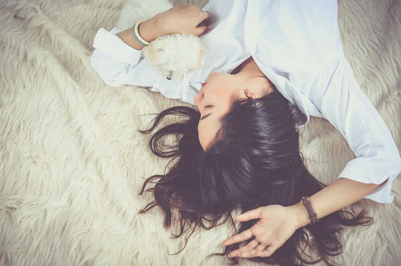Woman relaxing on fluffy white rug with small white puppy
